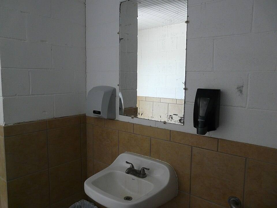 Small coastal Florida bath with a white toilet, wall-hung sink, paper roll, and a bright window over the tank