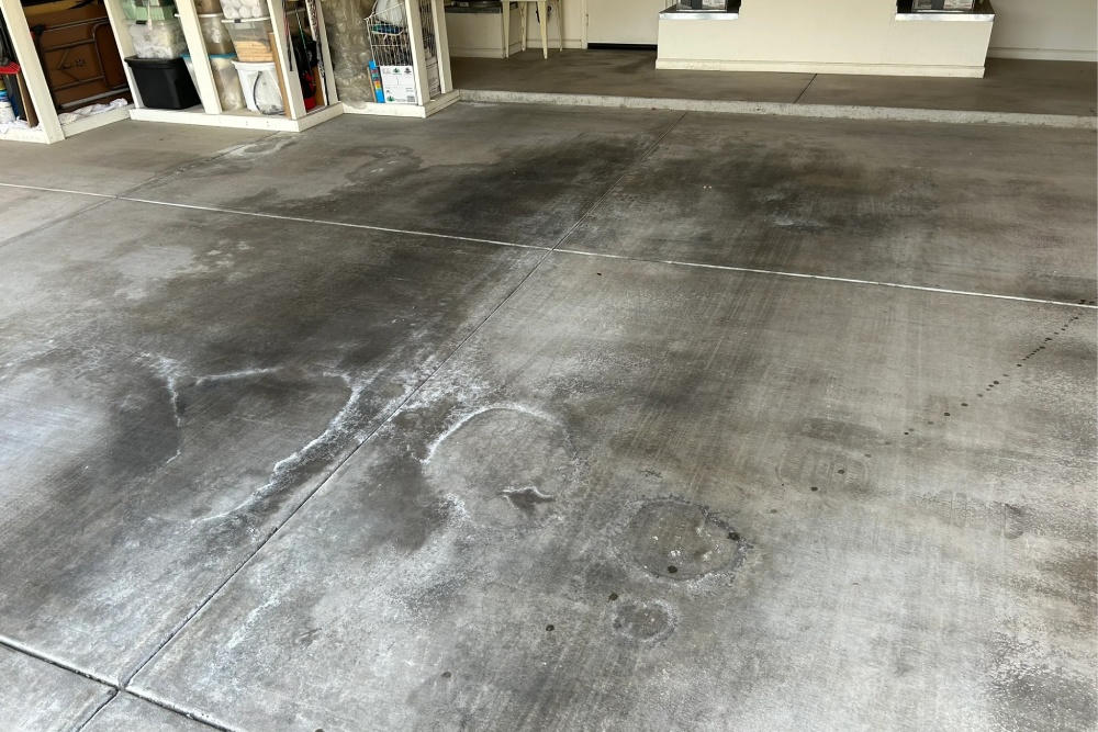 Coastal Florida attached garage concrete floor with moisture marks in morning light, storage shelves along the wall, open door area visible, no people and no text