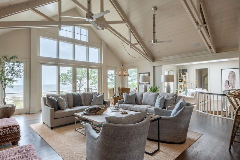 Coastal Florida condo living room with large glass doors facing the water in soft morning light, upholstered seating on a rug, no people and no text